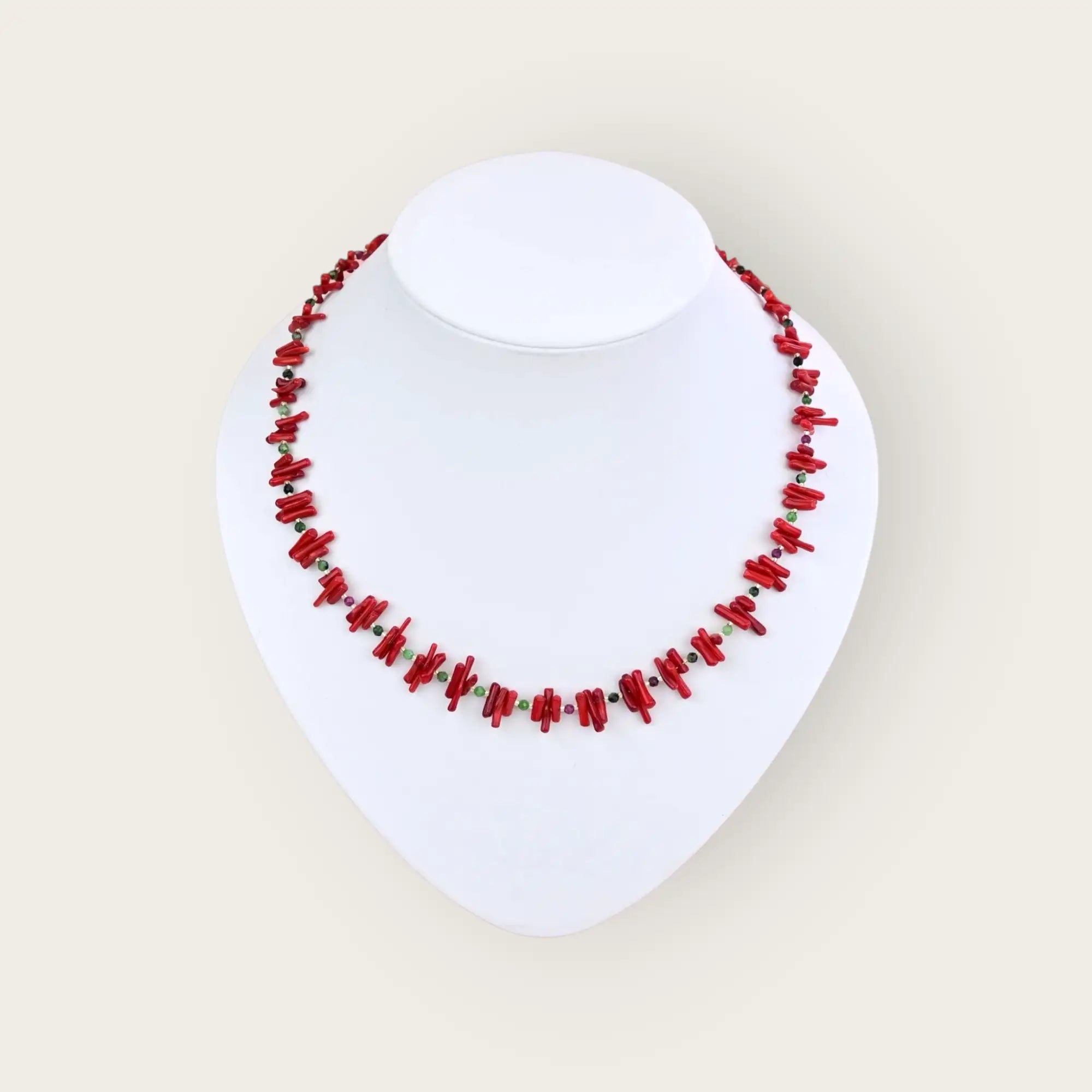 Eine leuchtend rote Korallenkette mit dazwischenliegenden dunklen und grünen Perlen, ausgestellt auf einem weißen Schaufensterpuppen-Torso.